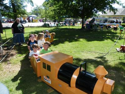 children riding a yellow train with an adult in the background
