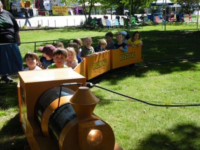 children riding a yellow train with chairs and trees in the background