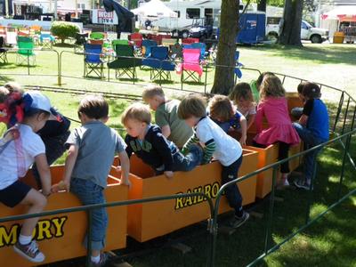 children riding a yellow train with chairs and trees in the background