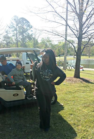 teen girl proudly holds a fish in front of a golf cart with a man and a boy inside