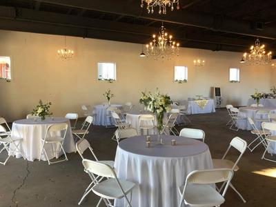 A spacious room featuring white tables and chairs arranged neatly for gatherings or meetings.